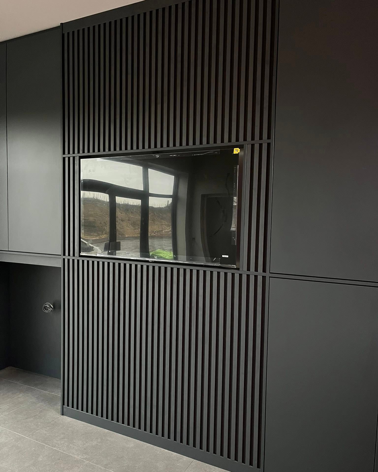 Black media wall with slatted panelling around the TV