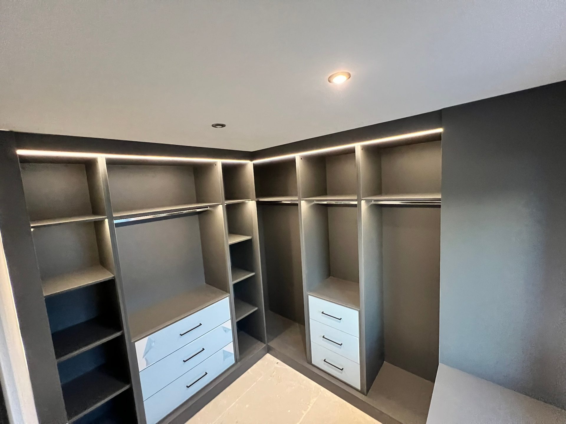 Grey walk-in wardrobe with LED strips over the hanging rails