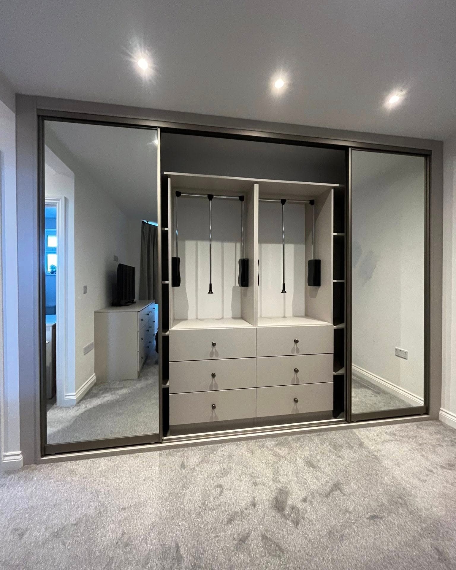 Mirrored sliding wardrobe open to show drawers and hanging space