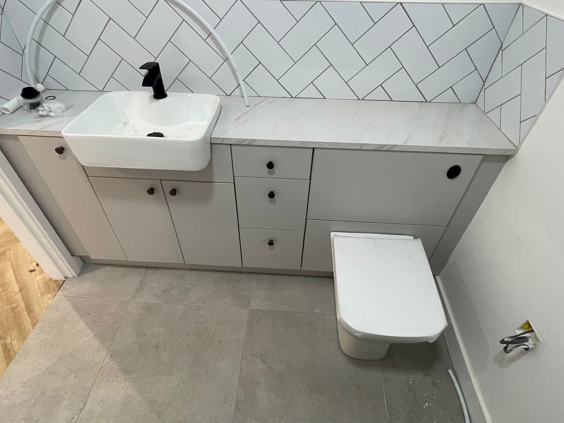 Light grey bathroom vanity, drawers and toilet unit under one marble-effect worktop