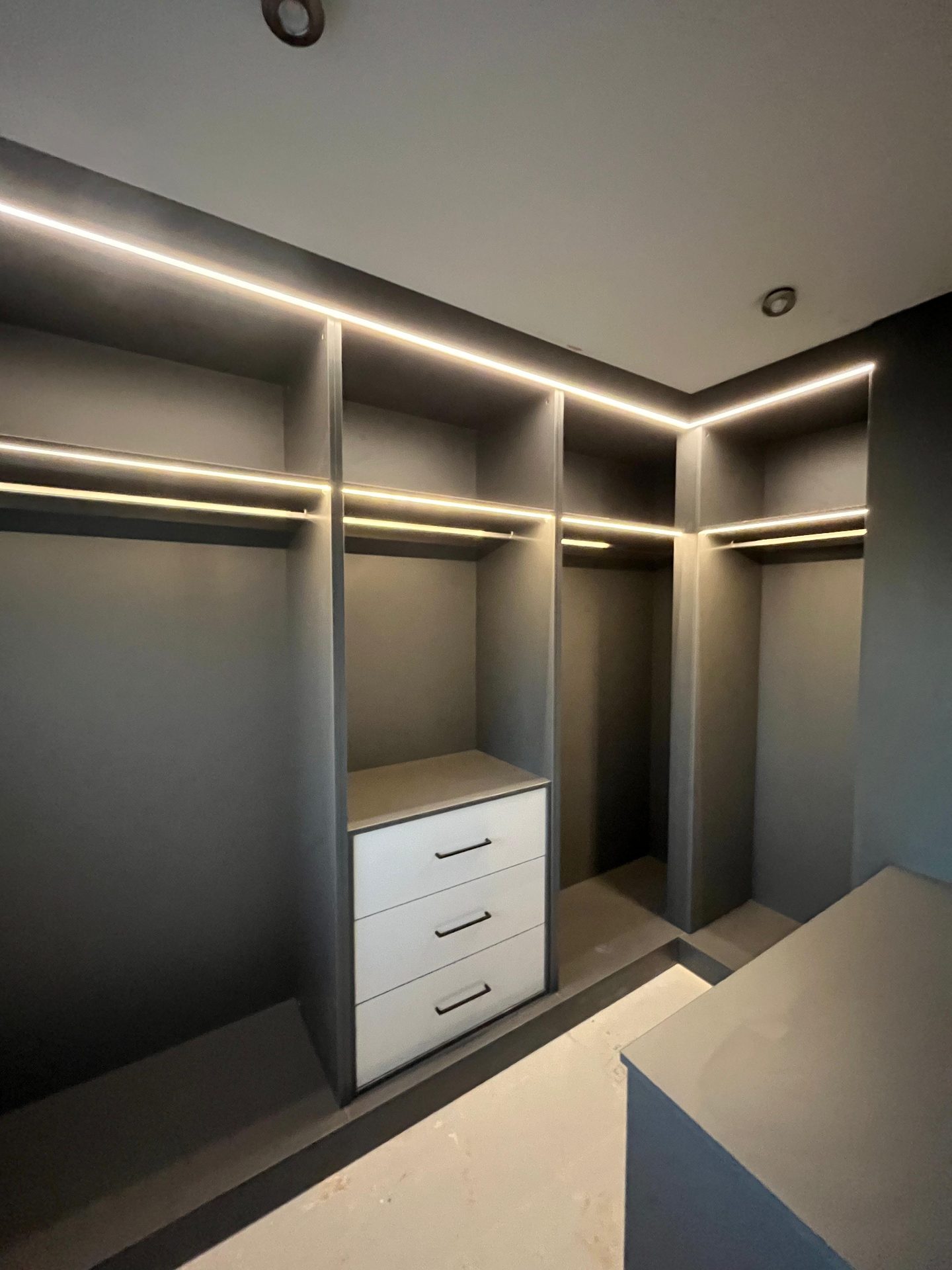 Walk-in wardrobe with lit hanging and light grey drawers