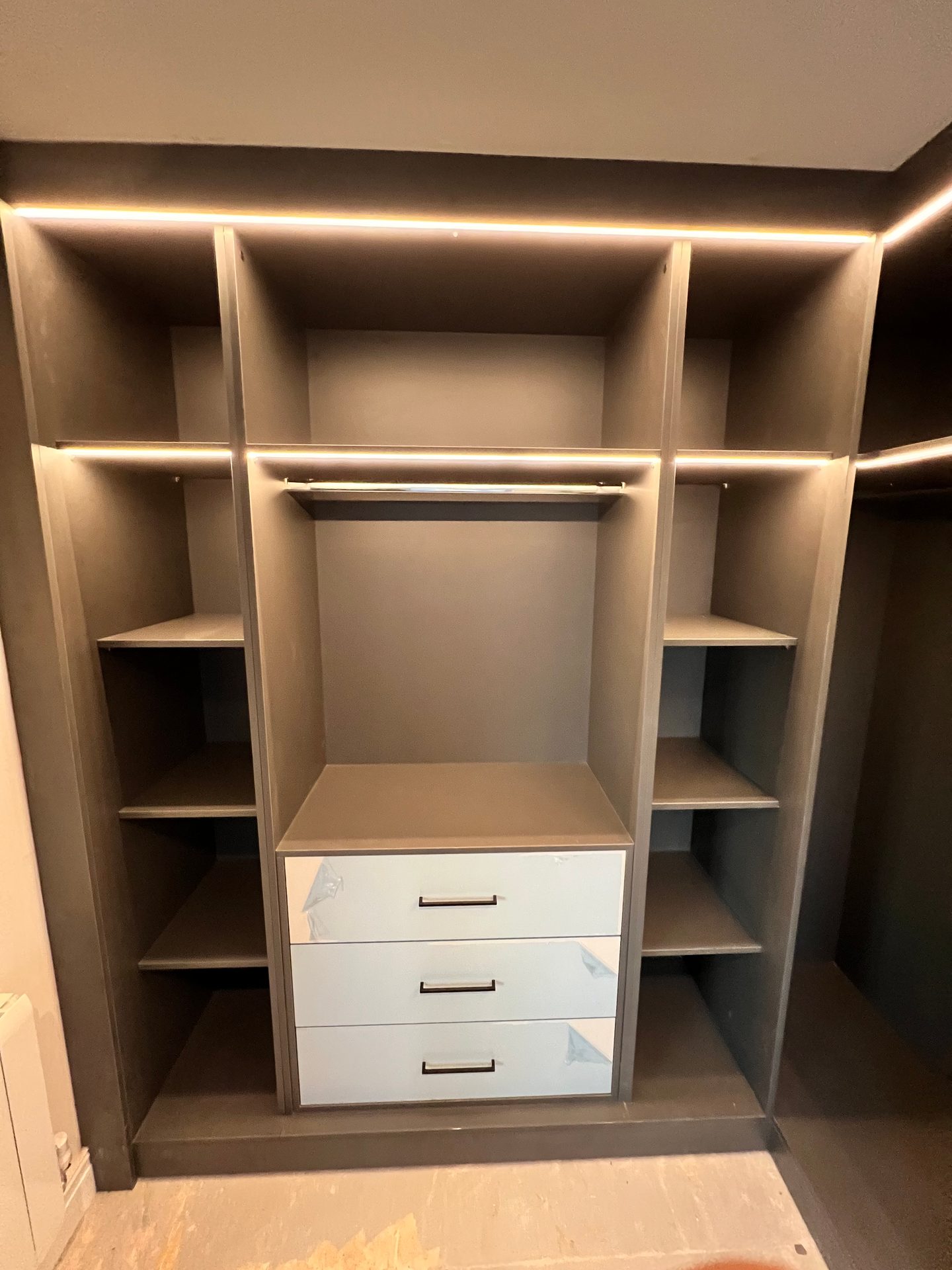 Walk-in wardrobe section with a lit rail, shelves and drawers